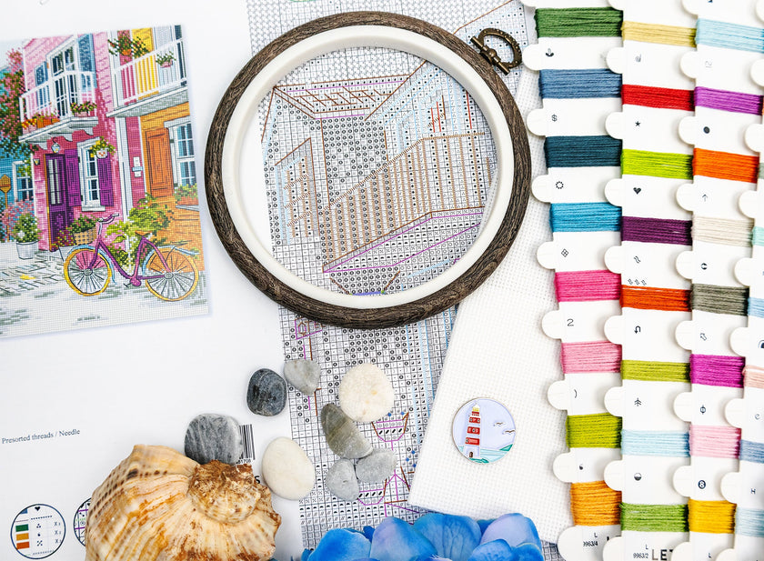 Embroidery hoop with a partially completed design, colorful threads, and seashells on a table.