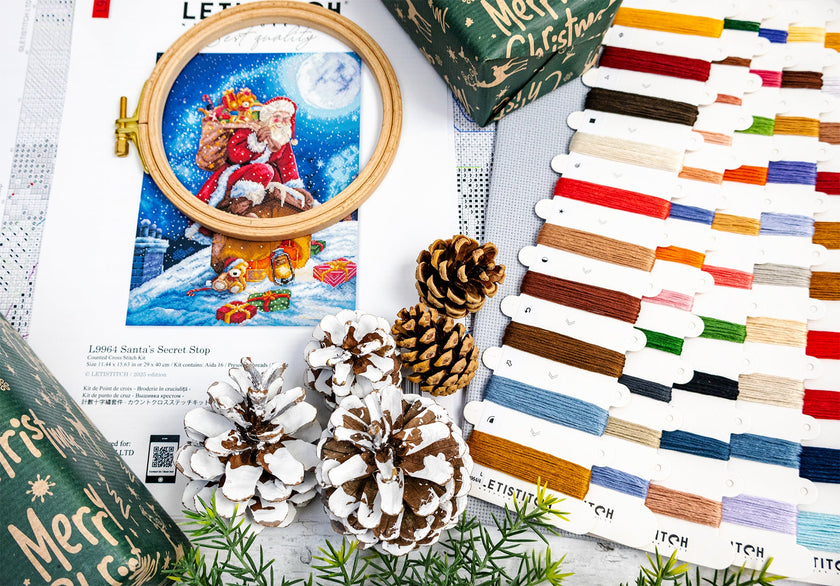 Embroidery hoop with Santa Claus design, thread colors, and Christmas-themed packaging on a white surface.