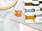 Cross-stitching materials including a hoop, thread, and a small decorative item on a cross-stitch chart.