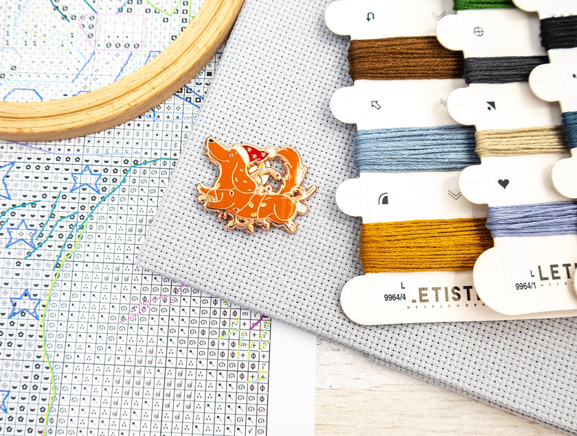 Cross-stitching materials including a hoop, thread, and a small decorative item on a cross-stitch chart.