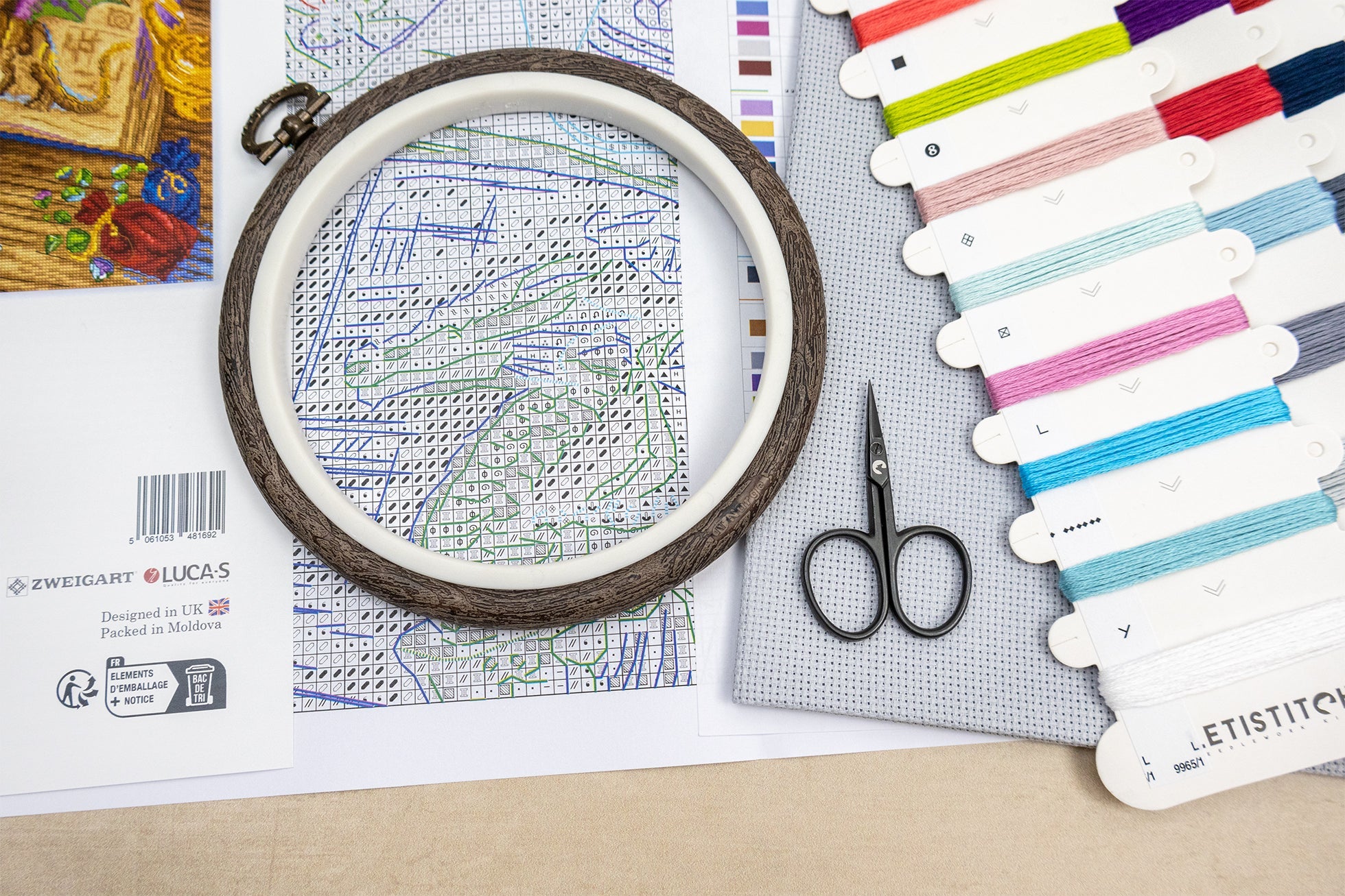 Embroidery hoop with cross-stitch pattern, scissors, and color swatches on a flat surface