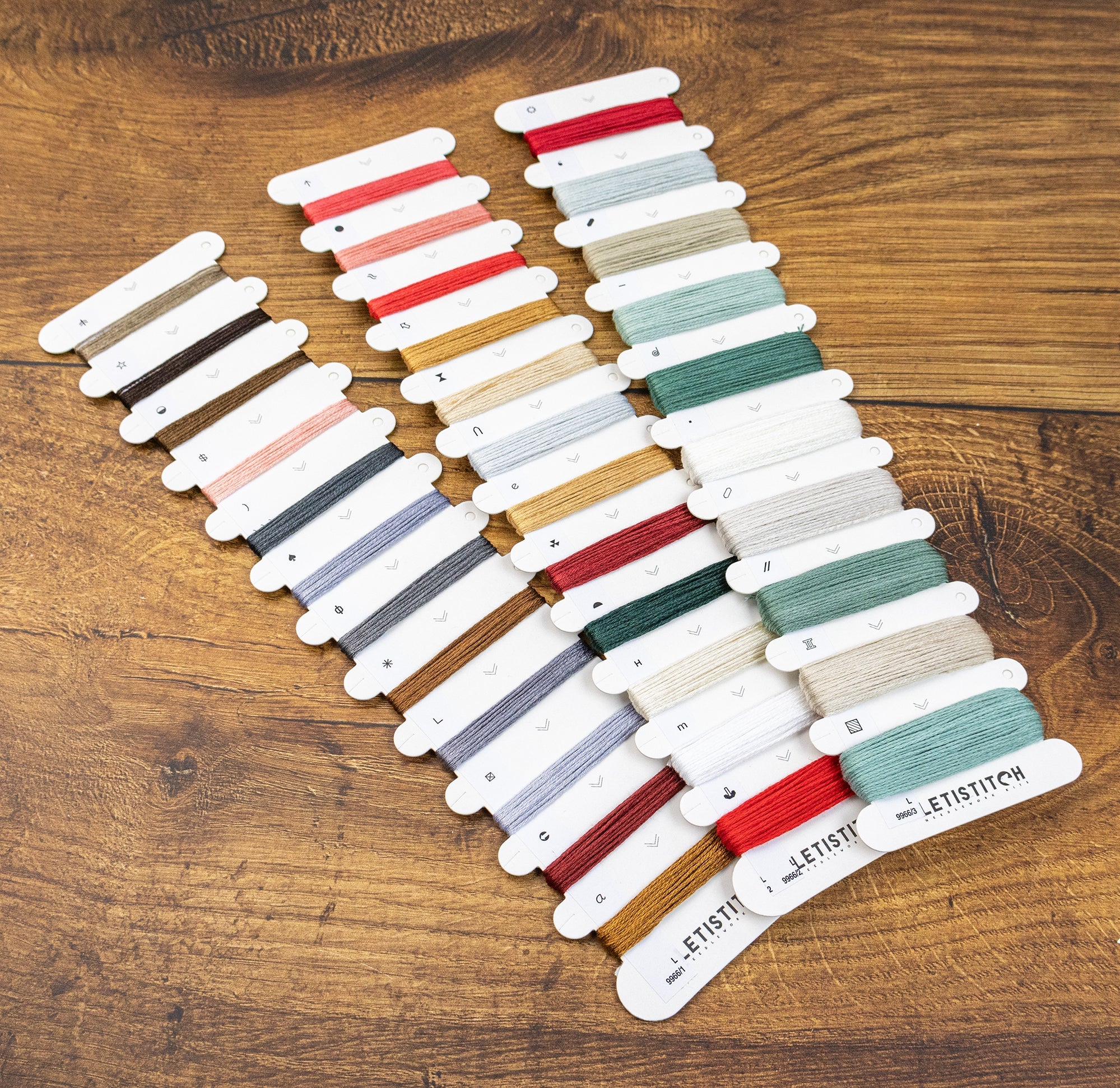 Set of colorful thread spools on a wooden surface with 'Leistitch' branding.