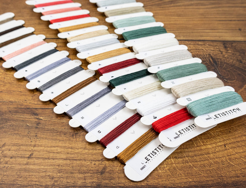 Color swatch cards with embroidery threads on a wooden surface