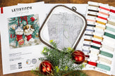 Cross-stitch kit with hoop, thread, and pattern sheet on a wooden surface.