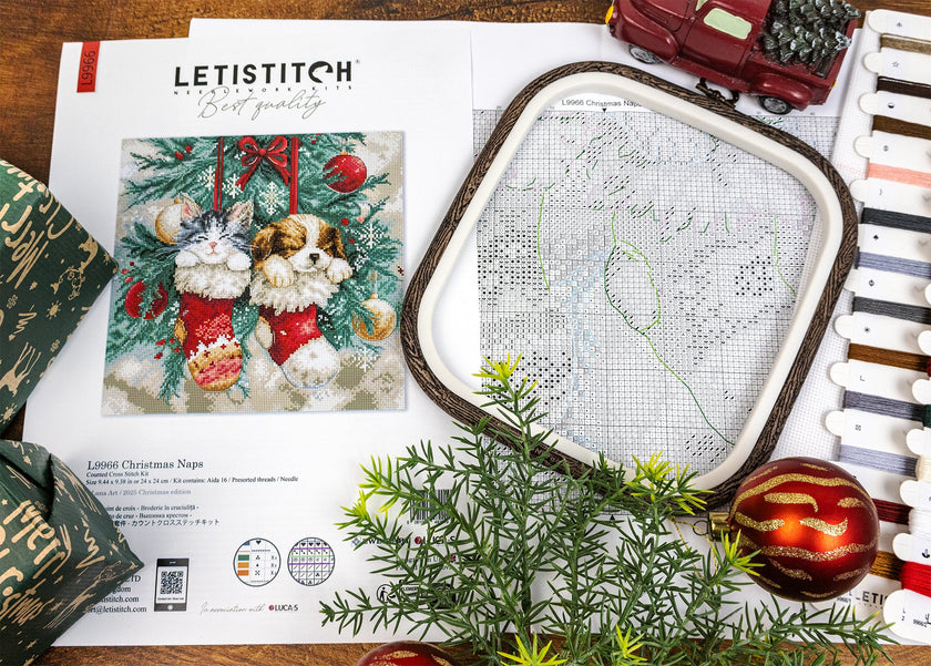 Cross-stitch kit with embroidery hoop, pattern, and festive decorations on a wooden surface.