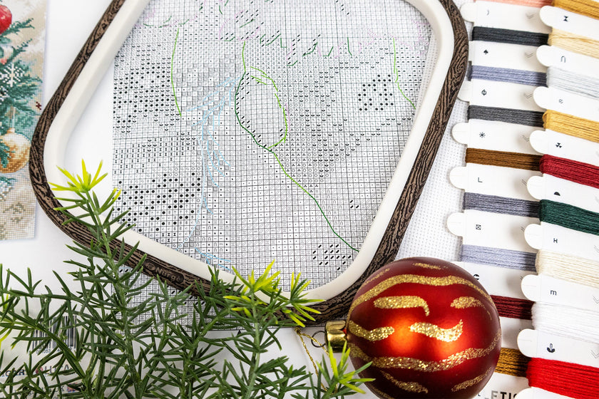 Embroidery hoop with cross-stitch pattern, red ornament, and thread spools on a white background