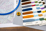 Color swatches from Letistitch with a map and badge on a wooden surface