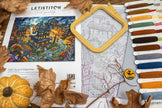 Cross-stitching kit with fabric, threads, and a pumpkin decoration on a wooden surface.