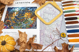 Cross-stitching kit with fabric, hoop, threads, and a pumpkin-themed picture on a table.