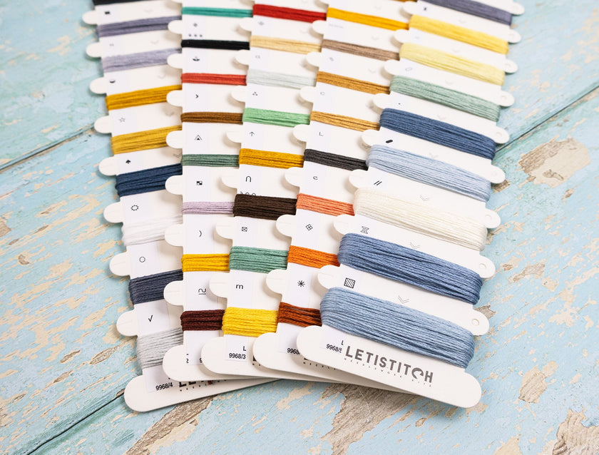 Collection of colorful embroidery floss on white cards with 'LetiStitch' branding on a light blue wooden surface.