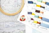 Cross-stitching kit with embroidery hoop, thread, and pattern sheet on a white background