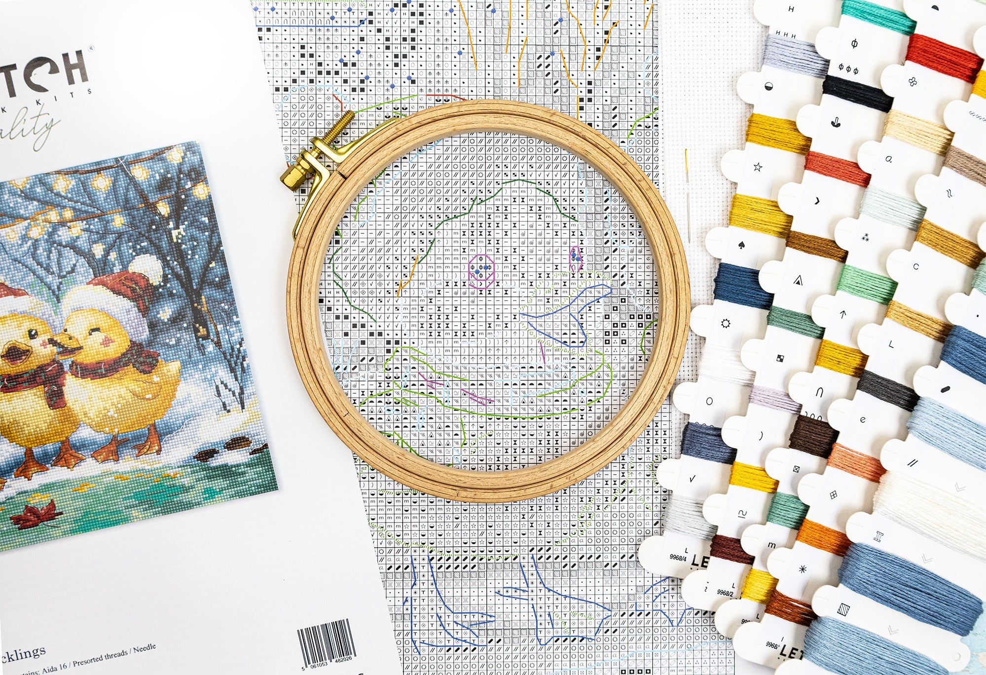 Cross-stitching kit with embroidery hoop, pattern, and color chart on a white surface.