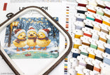 Cross-stitch kit with three yellow chicks in winter hats and scarves, surrounded by embroidery threads and color swatches.