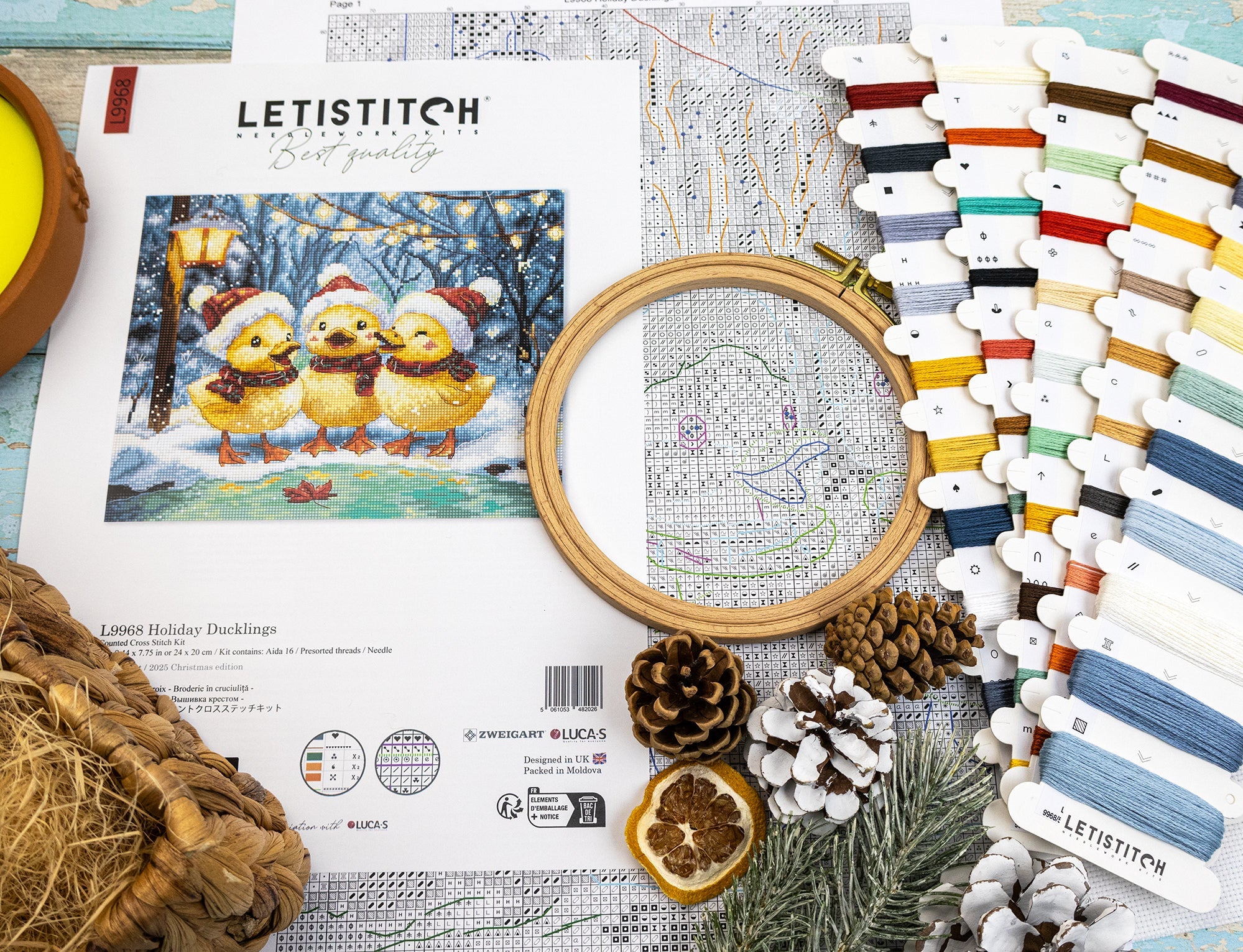 Cross-stitch kit with embroidery hoop, thread, and design sheet on a wooden surface.