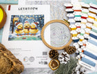 Cross-stitch kit with embroidery hoop, thread, and design sheet on a wooden surface.