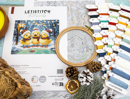 Cross-stitch kit with embroidery hoop, thread, and design sheet on a wooden surface.