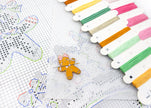 Colorful embroidery floss spools with a gingerbread man pin on a cross-stitch pattern.