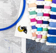 Colorful embroidery thread spools with a cross-stitch hoop and fabric in the background