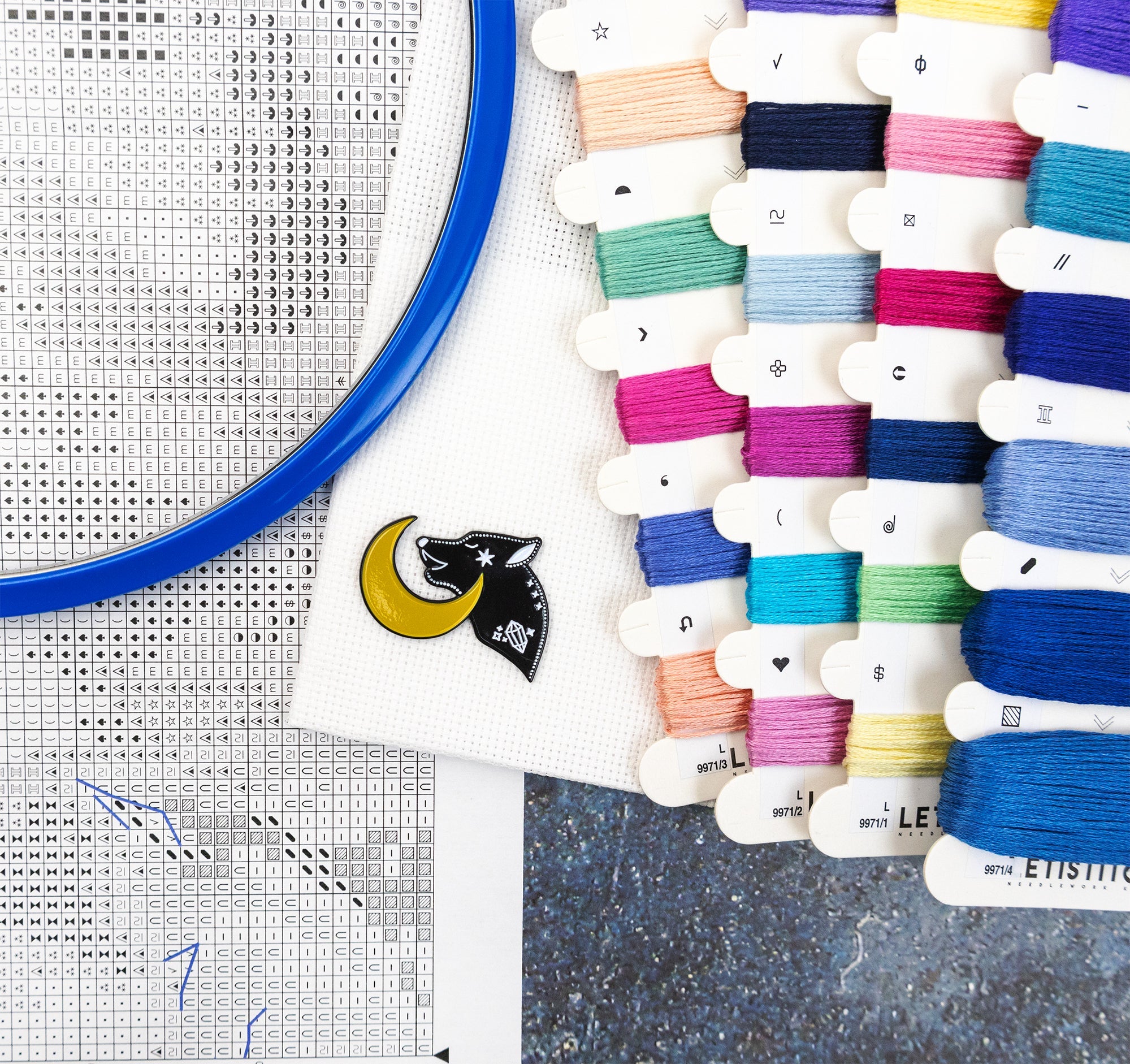 Colorful embroidery thread spools with a cross-stitch hoop and fabric in the background