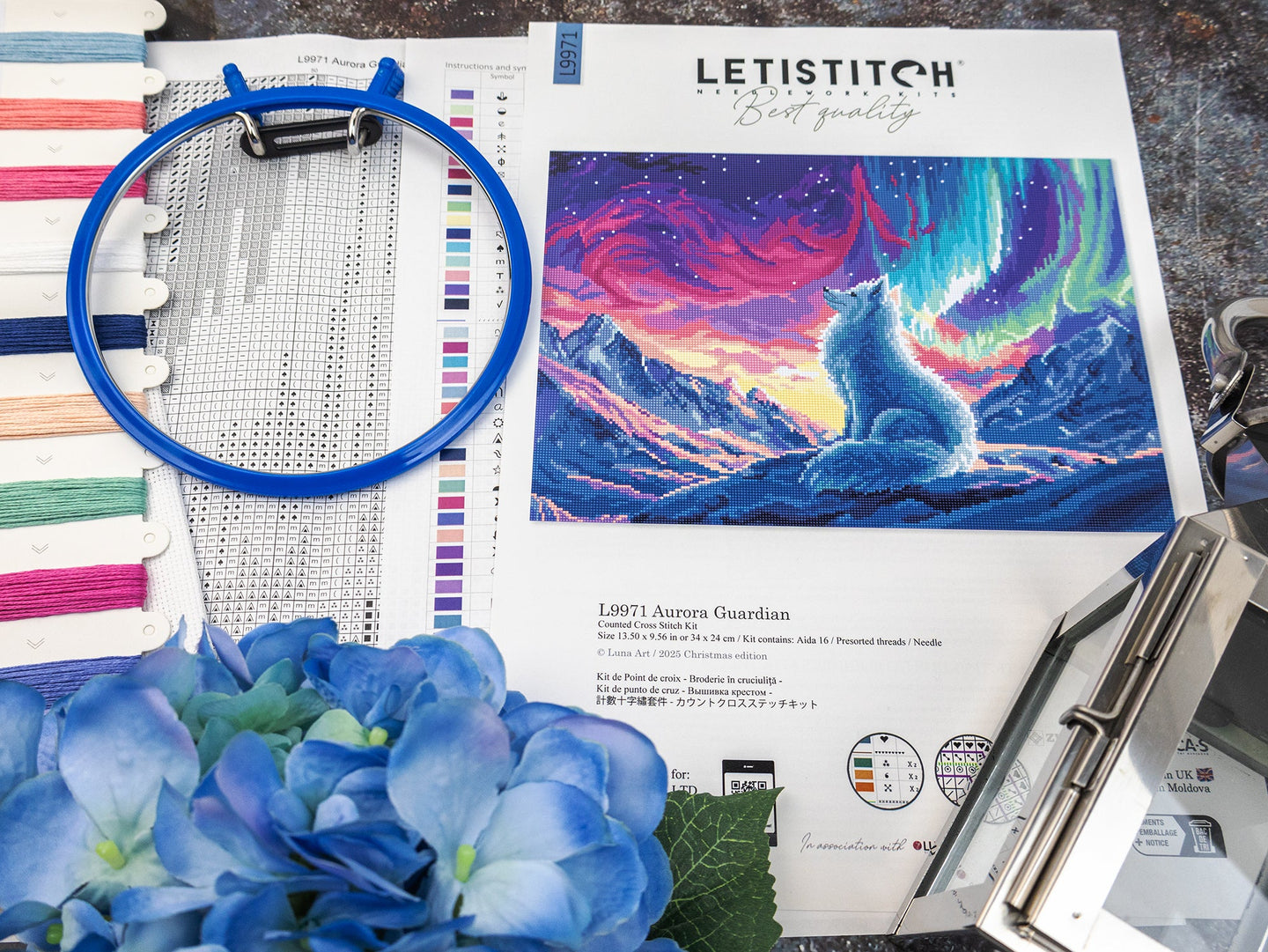 Embroidery hoop, thread spools, and a cross-stitch pattern of a wolf under an aurora borealis sky.
