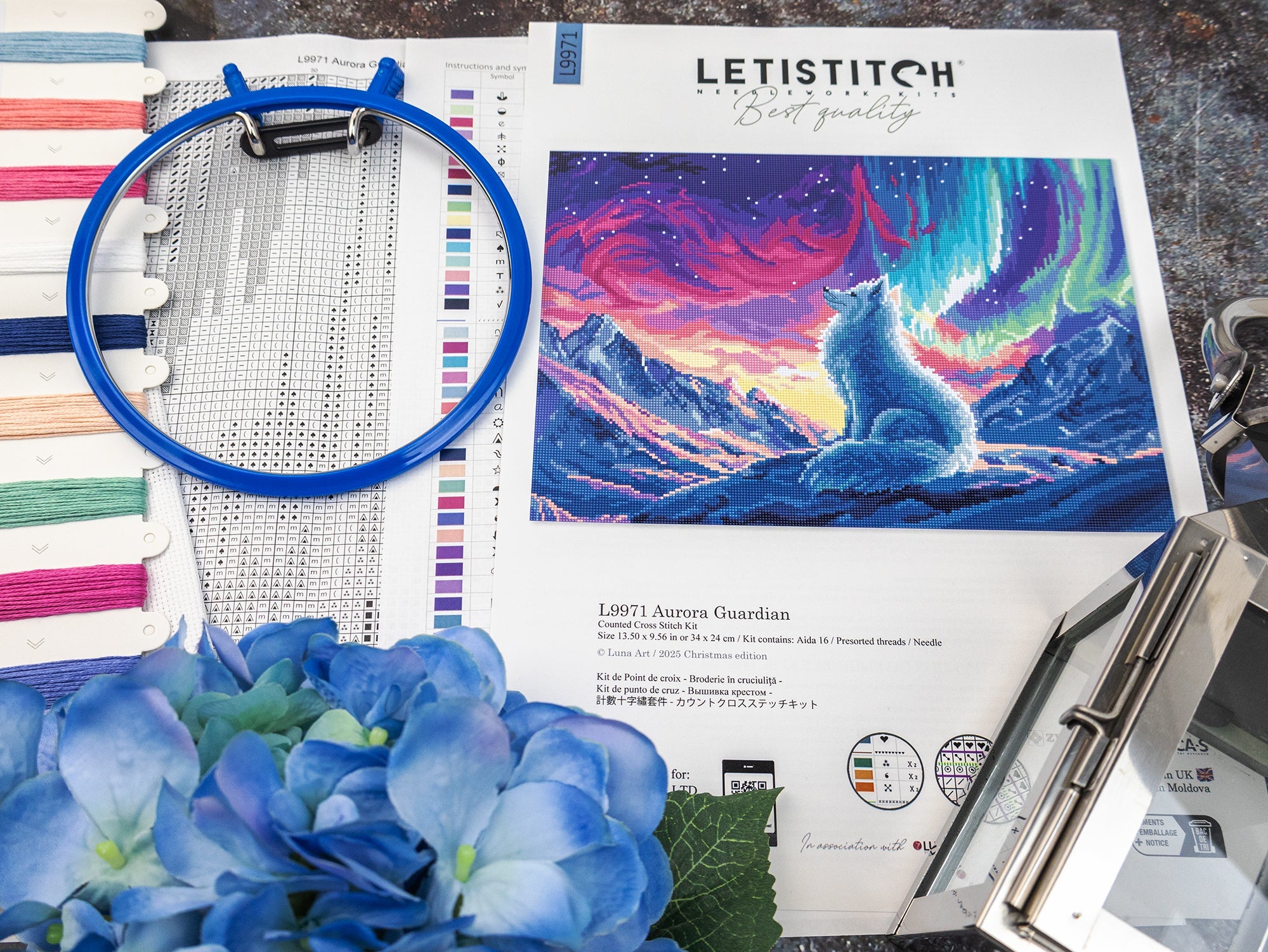 Embroidery hoop, thread spools, and a cross-stitch pattern of a wolf under an aurora borealis sky.