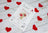Cross stitch kit with a teddy bear design surrounded by red hearts on a wooden surface