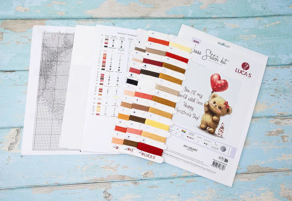 Cross stitch kit with pattern, color chart, and teddy bear design on a wooden surface