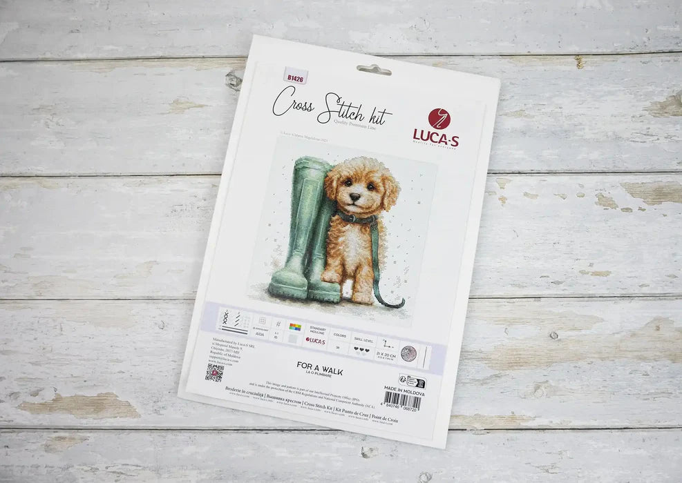 Cross stitch kit packaging with a dog and boot illustration on a wooden surface
