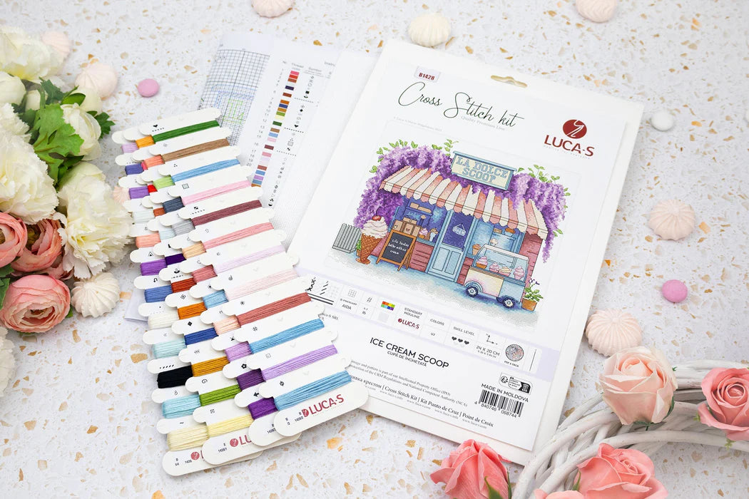 Cross stitch kit with colorful threads and packaging on a decorative surface with flowers.