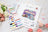 Cross stitch kit with colorful threads and packaging on a decorative surface with flowers.