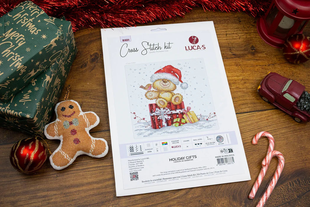 Cross-stitch kit with Christmas-themed design on a wooden surface with festive decorations.