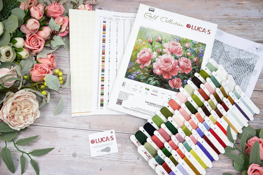 Embroidery kit with floral pattern, threads, and color chart on a wooden surface.