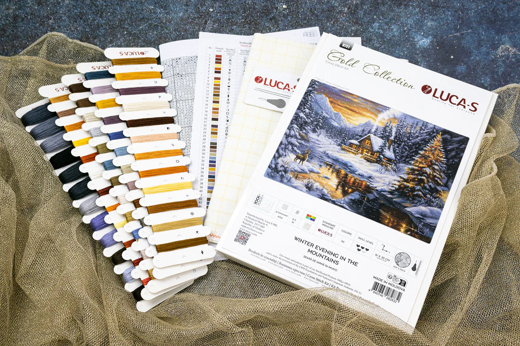 Set of embroidery threads and a design book titled 'Winter Evening in the Mountains' by Lucas on a textured surface.