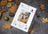 Cross stitch kit by Lucas on a gray surface with autumn leaves and pine cones.
