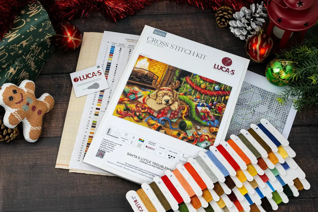 Cross stitch kit with colorful threads and Christmas-themed design on a wooden surface.