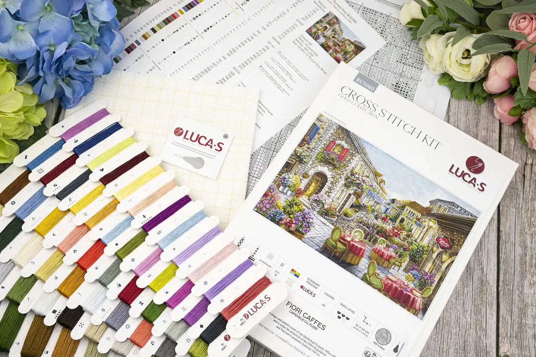 Cross stitch kit with threads, pattern, and design illustration on a wooden surface.