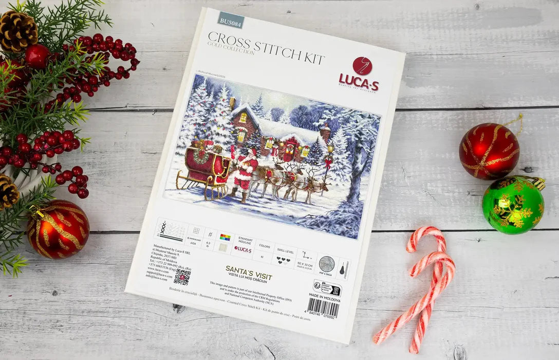 Lucas cross-stitch kit packaging with Christmas-themed design on a wooden surface with decorations.