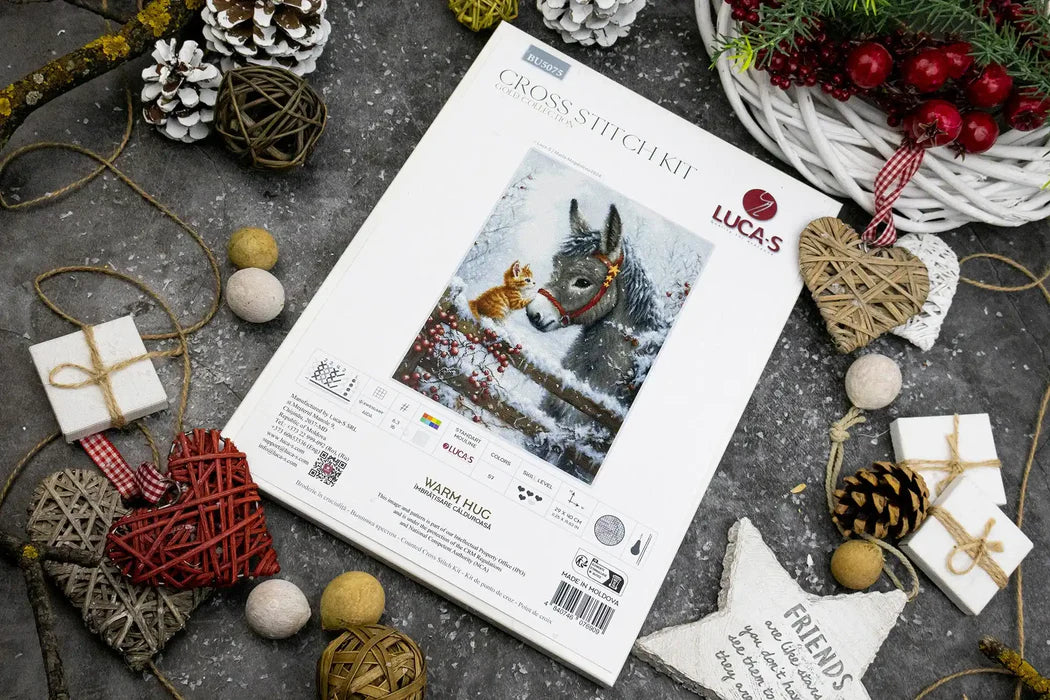 Cross-stitch kit with a donkey design surrounded by Christmas decorations on a textured surface.
