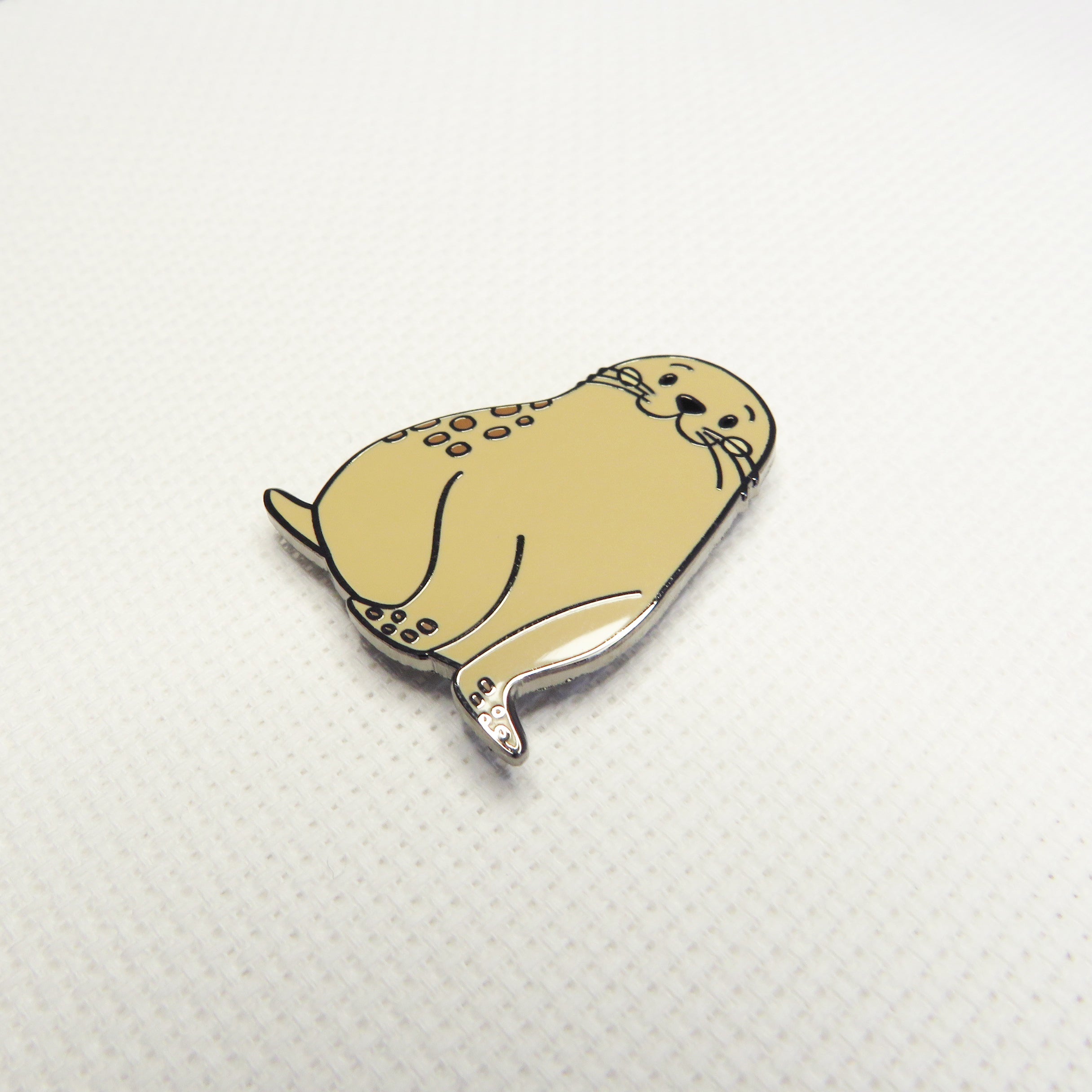 Beige seal-shaped pin on a white textured background