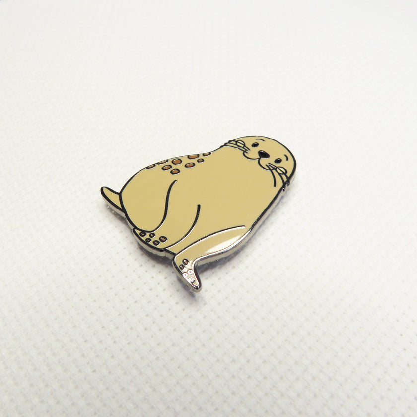 Beige seal-shaped pin on a white textured background