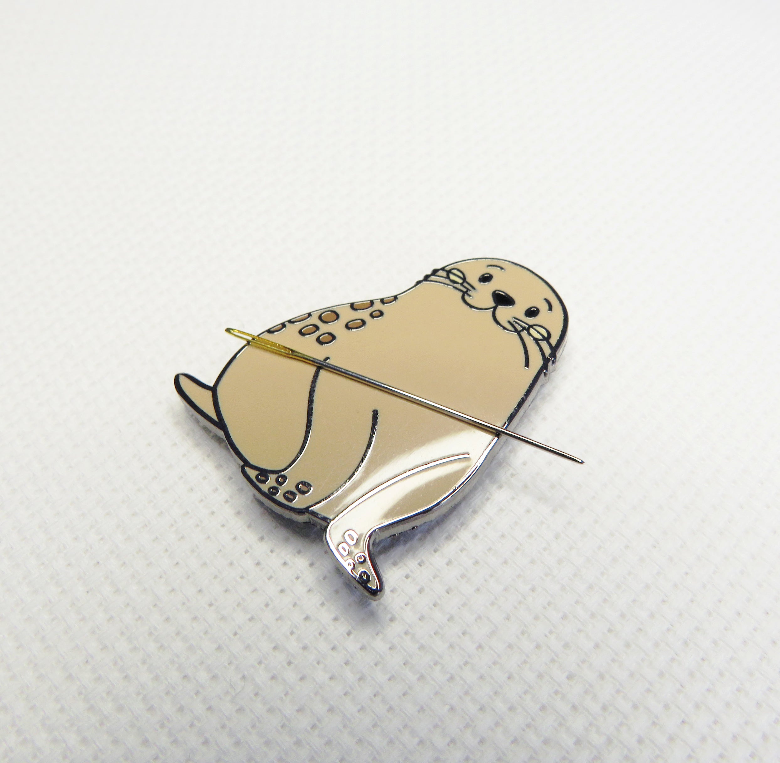 Seal-shaped brooch with a needle on a textured white backgrounds