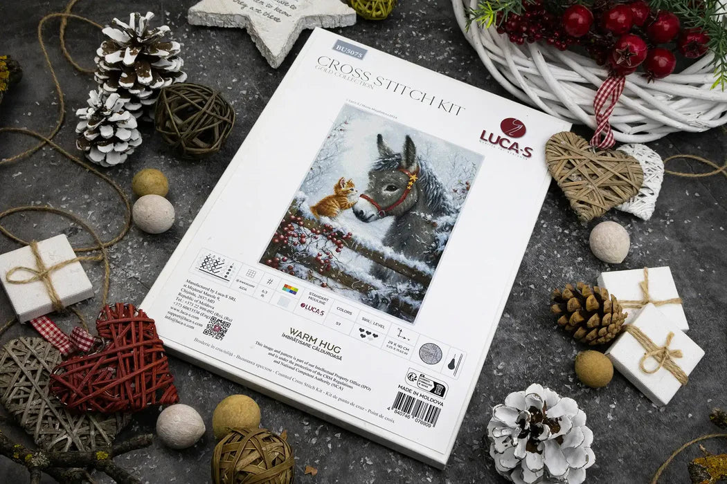 Lucas cross-stitch kit packaging with Christmas decorations on a dark surface