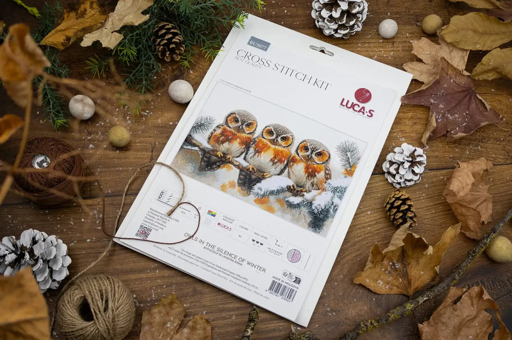 Lucas cross-stitch kit for three owls on a wooden surface with decorative elements.