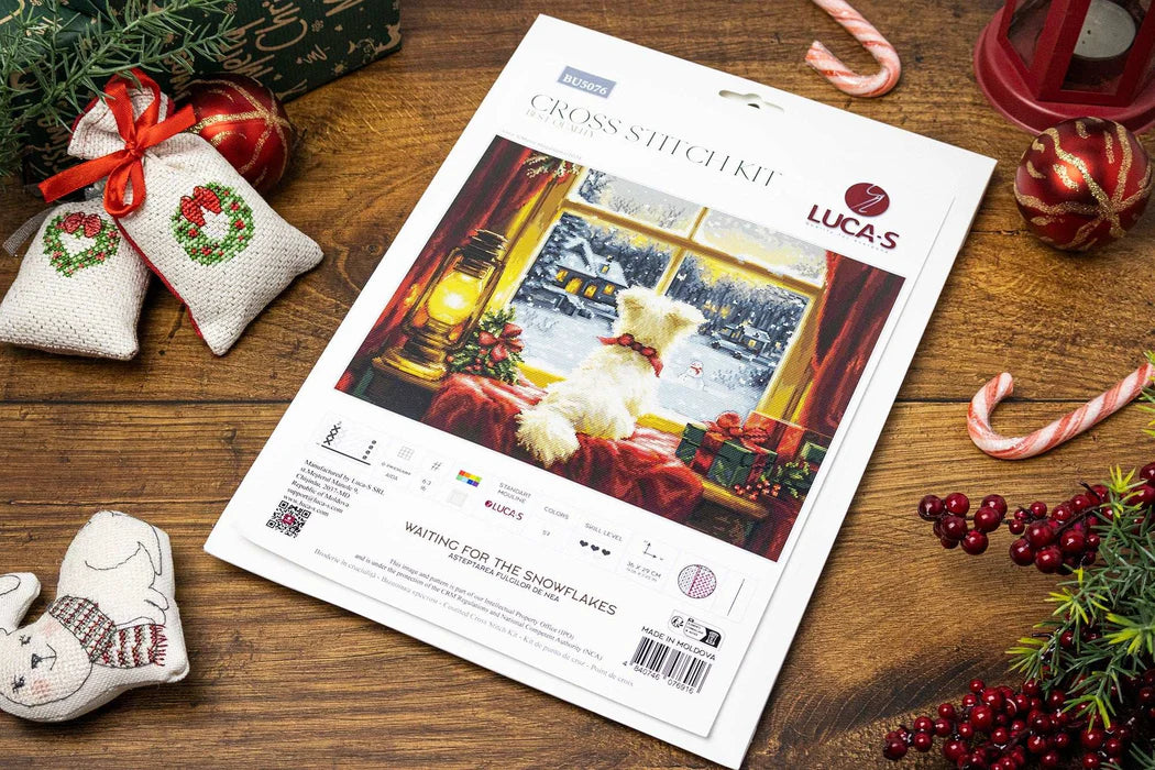 Lucas cross-stitch kit packaging on a wooden surface with Christmas decorations.