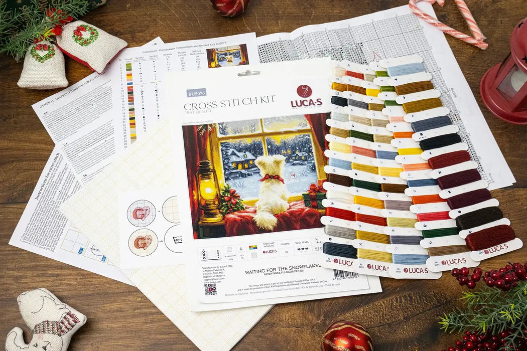 Cross stitch kit with color chart and pattern on a wooden table with Christmas decorations.