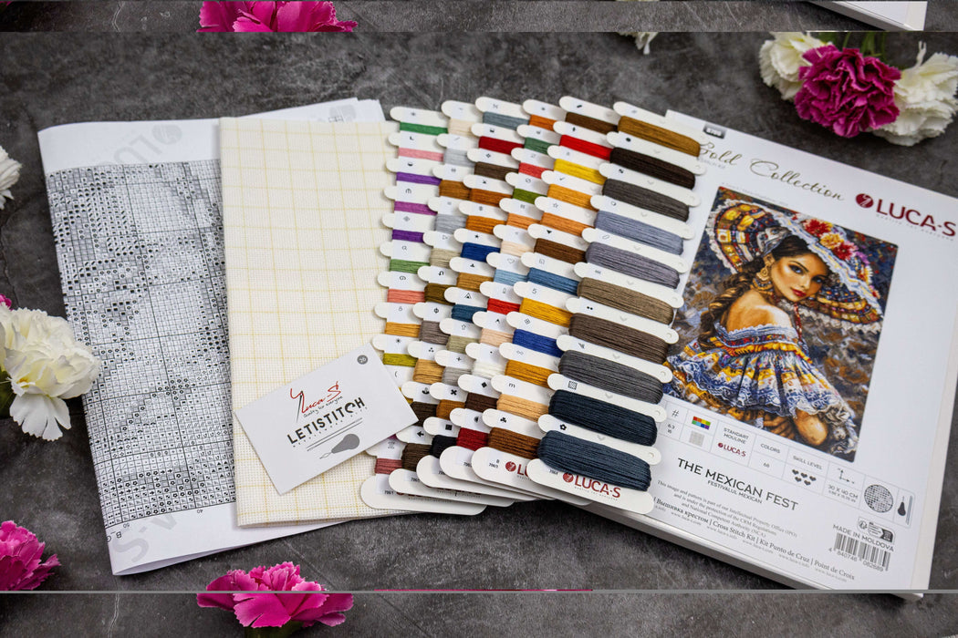 Color swatches and cross-stitch pattern book on a dark surface with flowers around