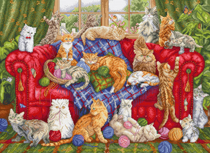 Cross-stitched scene of cats on a red chair with yarn and toys.