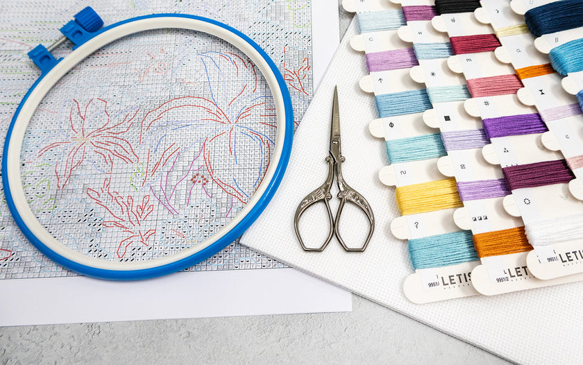 Embroidery hoop with floral pattern, scissors, and thread colors on a light surface