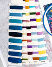 Color swatch card with various embroidery threads on a table with a patterned surface.