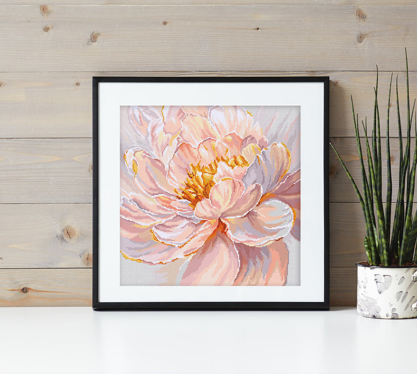 Framed artwork of a pink flower on a wooden wall with a plant.